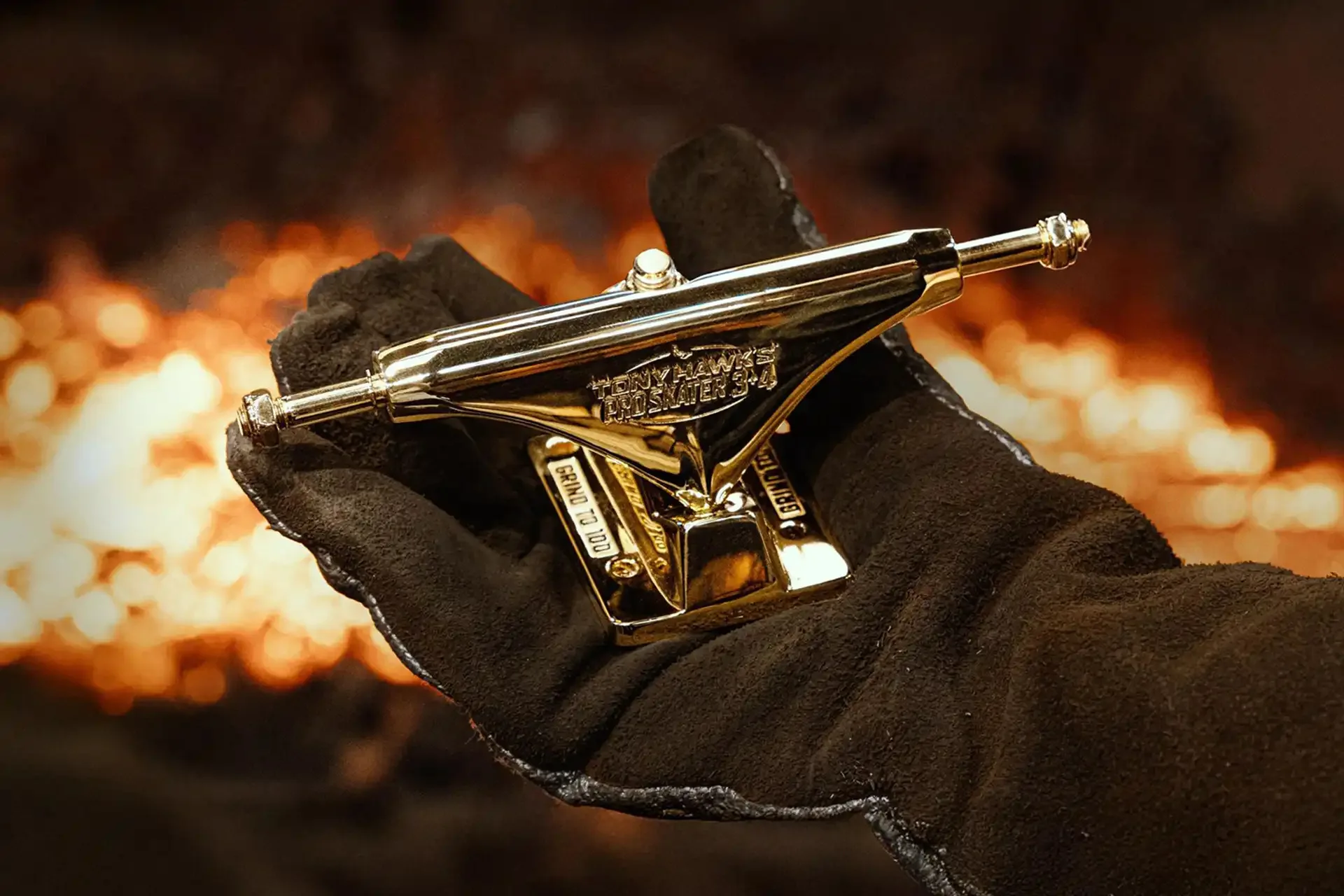 A gold-plated Tony Hawk’s Pro Skater 3+4 truck held in a leather foundry glove